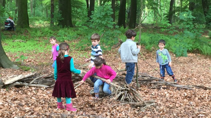 Die Kinder im Wald an einem Baumstamm.